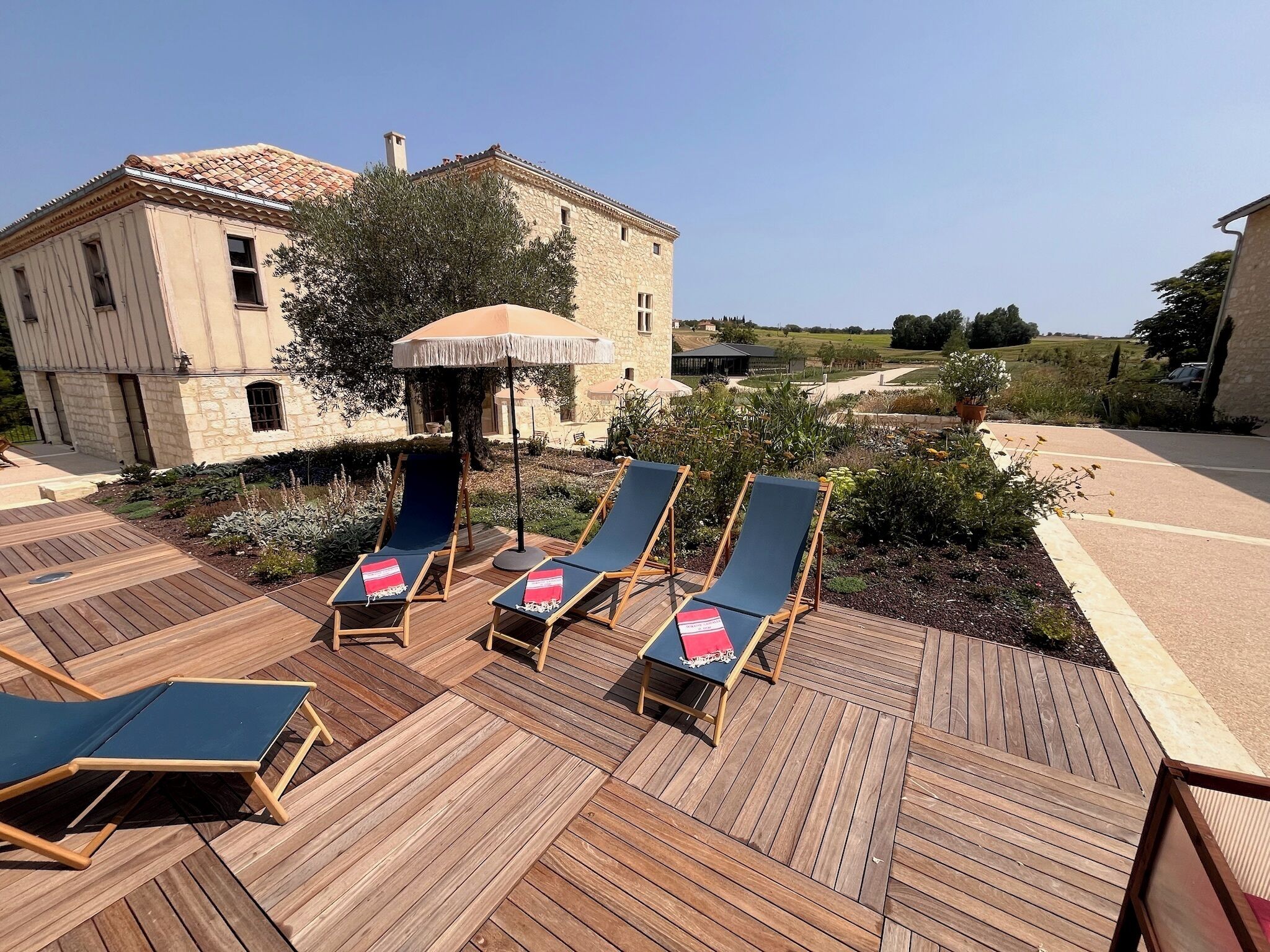 Una terraza de madera con sillones y una mesa, rodeada por un edificio de piedra con techo de tejas.