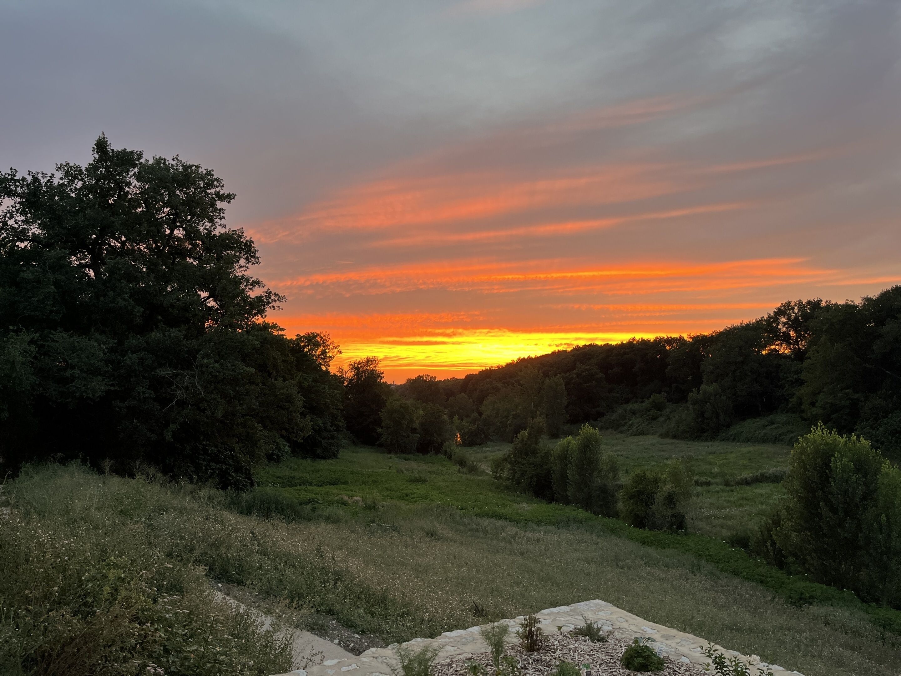 Un atardecer sobre un paisaje boscoso con una estructura de piedra en primer plano.