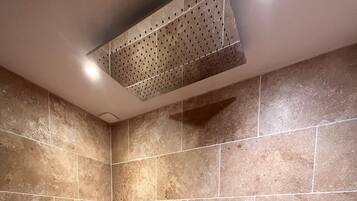 Un área de ducha con azulejos color beige, un cabezal de ducha de mano y un taburete pequeño.