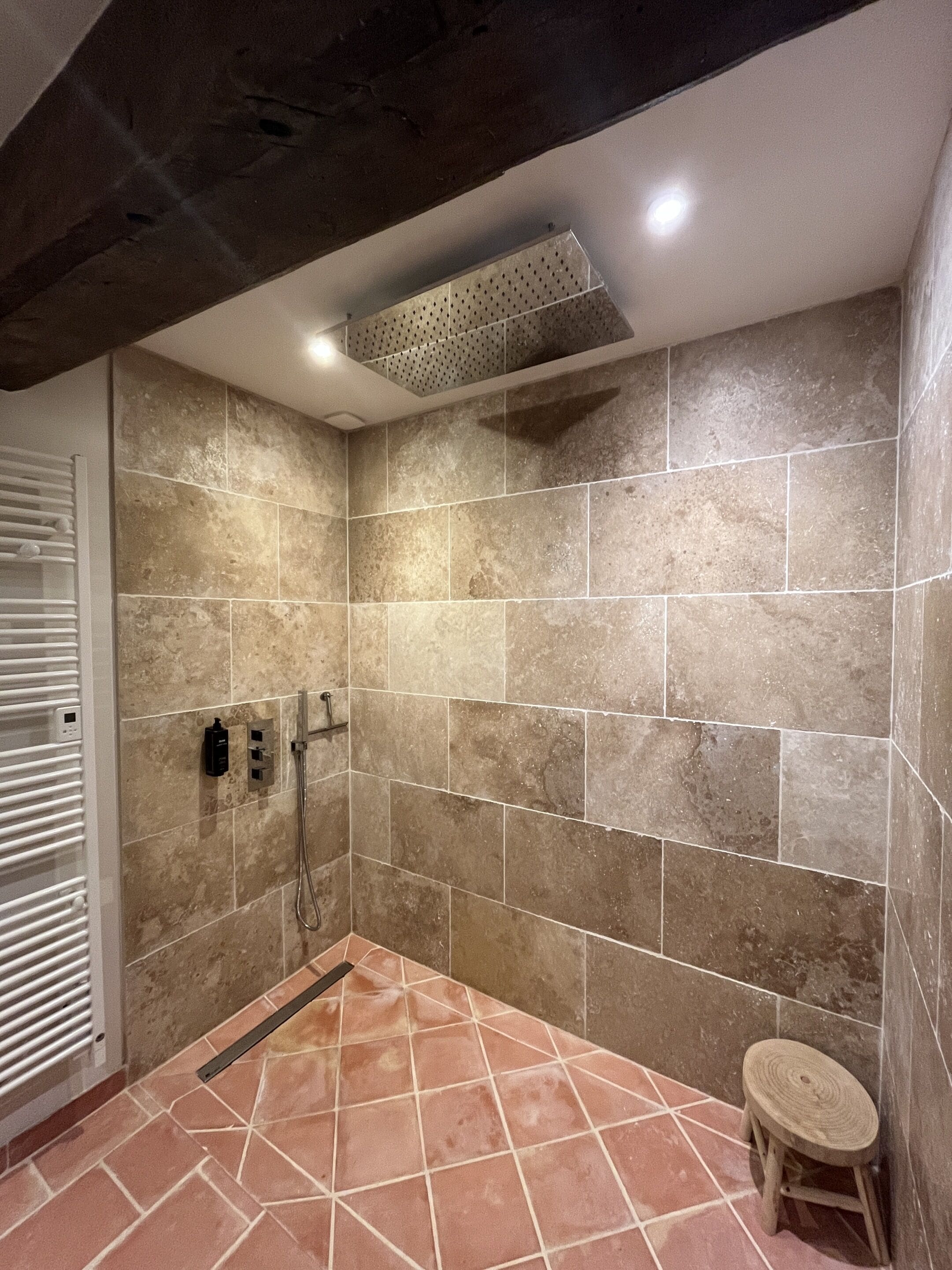 A modern bathroom with beige tiles, a shower, and a small stool.