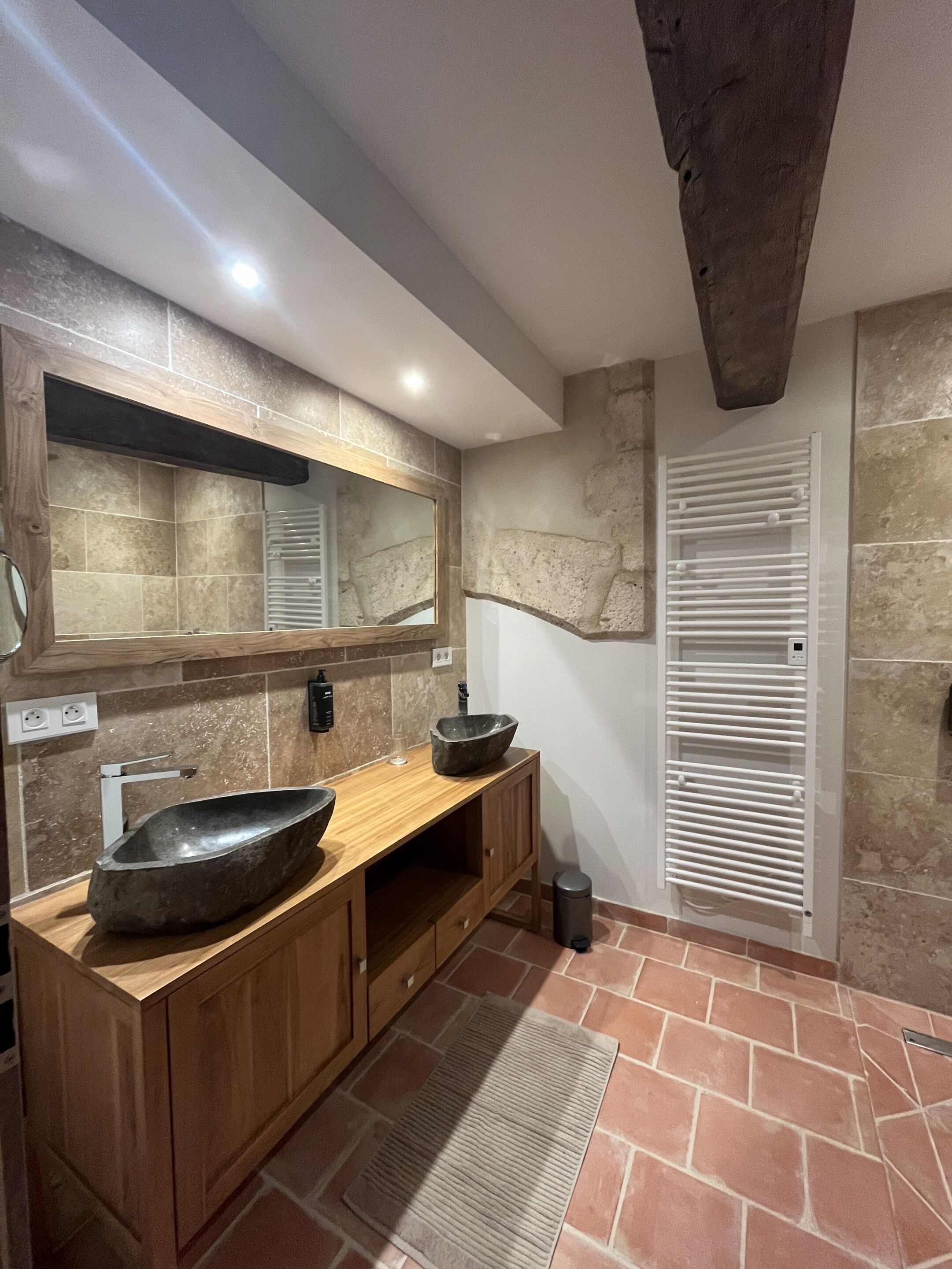 Un baño moderno con tocador de madera, un espejo grande, lavamanos de piedra y calefacción integrada.