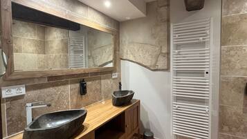 Un baño moderno con tocador de madera, un espejo grande, lavamanos de piedra y calefacción integrada.