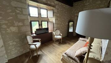 Una habitación con una cama, dos sillas, un escritorio con televisor y una ventana con vistas a árboles.