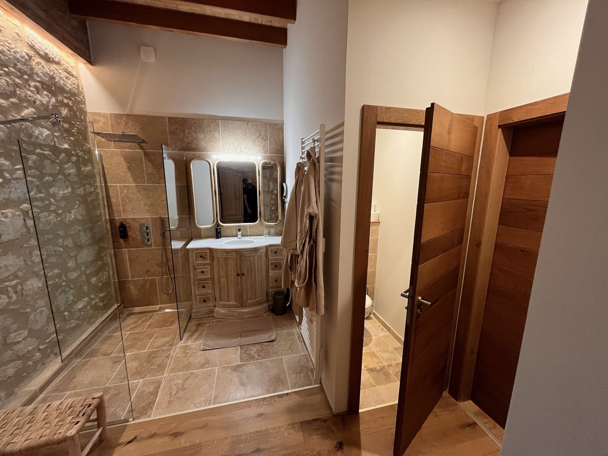Un baño moderno con ducha de piedra, tocador con espejo y puerta de madera.