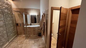 Un baño moderno con ducha de piedra, tocador con espejo y puerta de madera.