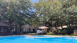 A swimming pool surrounded by trees and a building with outdoor seating. - Room in Lodge - Luxury Suite 1 in Boutique Lodge With Free Savannah Adventures 4x4 City Tour (Victoria Falls)