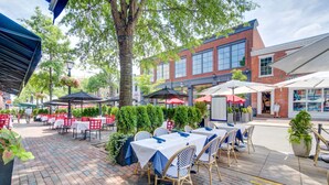 An outdoor dining area with tables and chairs, surrounded by brick walls and greenery. - HEART of Old Town! Historic 1BR! 99 Walk Score! (Alexandria)