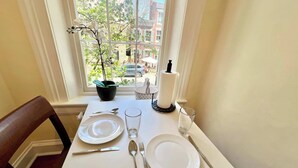 A dining table set with plates, cutlery, and a glass, positioned by a window with a view of buildings and greenery. - HEART of Old Town! Historic 1BR! 99 Walk Score! (Alexandria)
