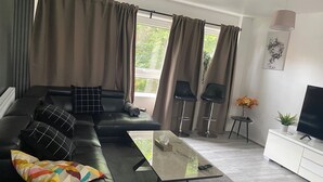 Una sala de estar moderna con un sofá de cuero negro, una mesa de centro de vidrio y dos taburetes negros.
