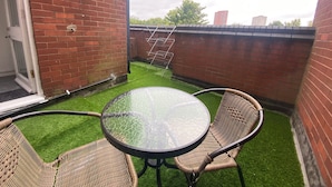 Un patio con una mesa de vidrio, sillas de mimbre, un muro de ladrillo y un tendedero.