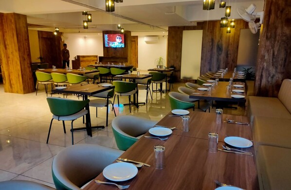 Restaurante com várias mesas e cadeiras, uma tela de televisão e detalhes em madeira.
