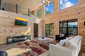 A spacious living room with a large TV, a fireplace, and a view of the outdoors. - Little Bear Lodge-new & private 3BR lodge in Cosby, mini golf, hot tub mtn views (Cosby)