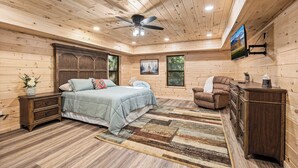 Ein Schlafzimmer einer Blockhütte mit einem Bett, einem Sessel, einer Kommode und einem Deckenventilator.