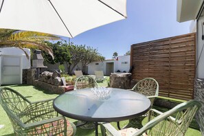 A patio with a round table and chairs, surrounded by a wooden fence, a white wall, and some greenery. - Bungalows Lapahi (San Bartolomé de Tirajana)
