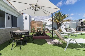 A patio with a round table and chairs, a large umbrella, and lounge chairs. - Bungalows Lapahi (San Bartolomé de Tirajana)