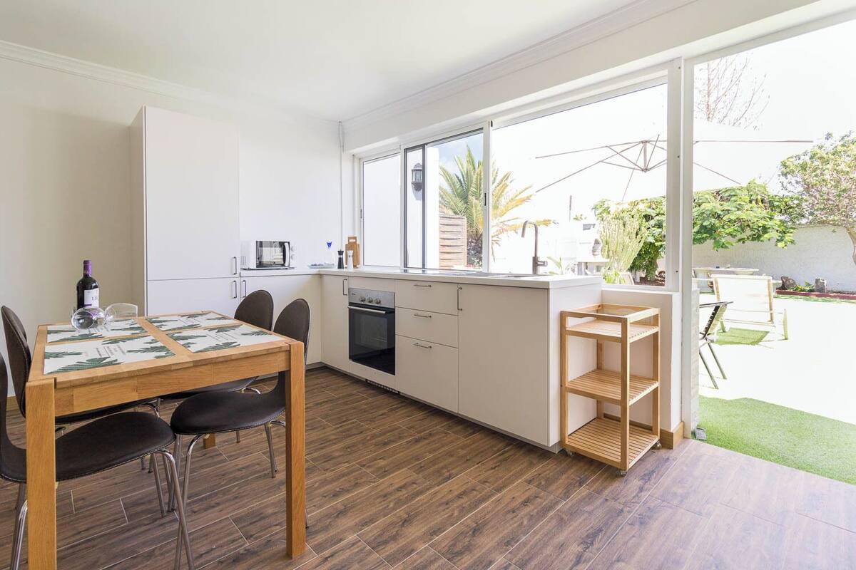 Uma cozinha moderna com armários brancos, forno embutido e janela com vista para um jardim.