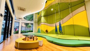 Un interno moderno con una zona relax dalle linee curve rivestita in verde, un pavimento in legno e una vista all'esterno attraverso ampie finestre.