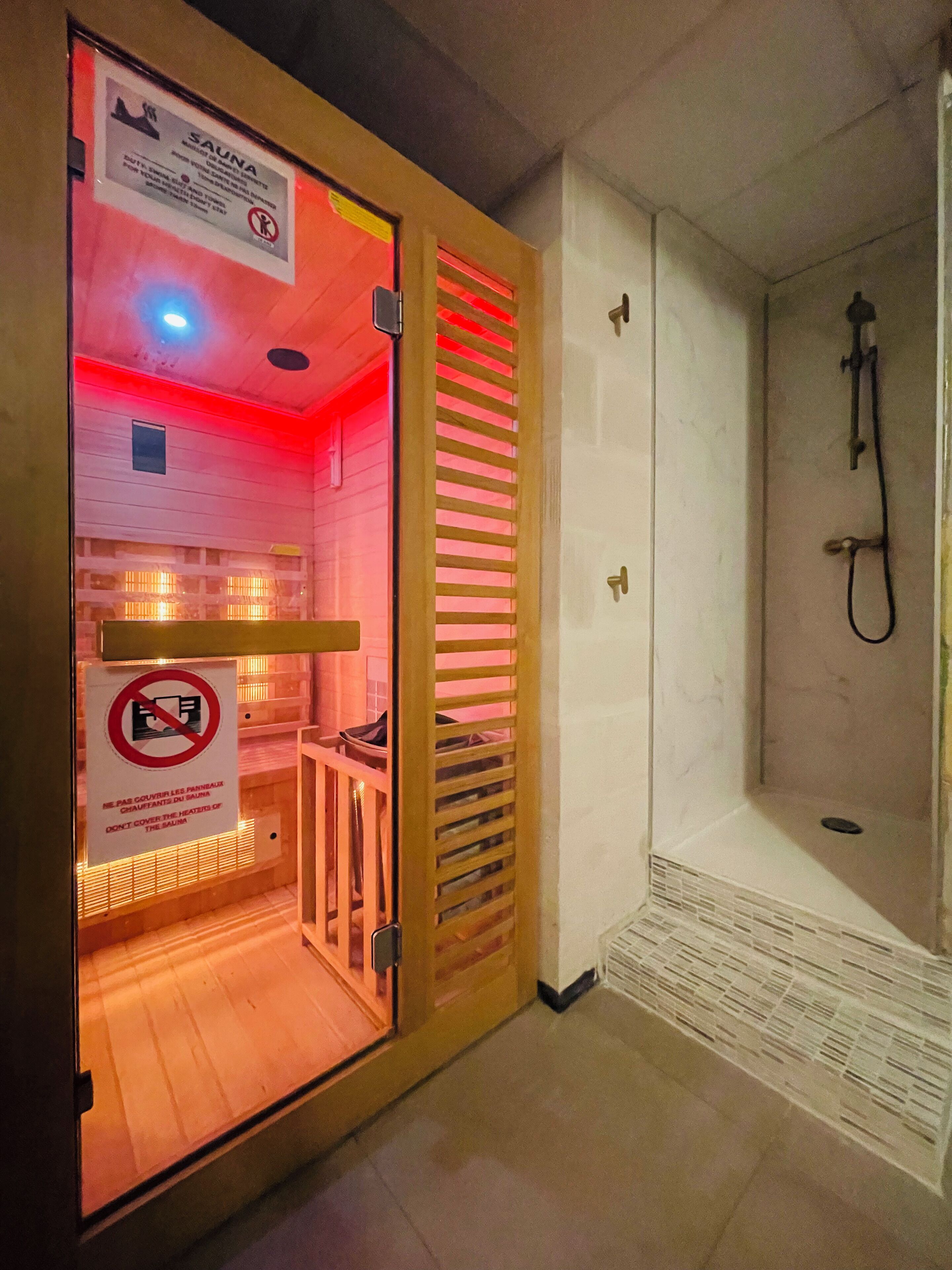 A sauna room with a wooden door, a shower area, and a sign with safety instructions.