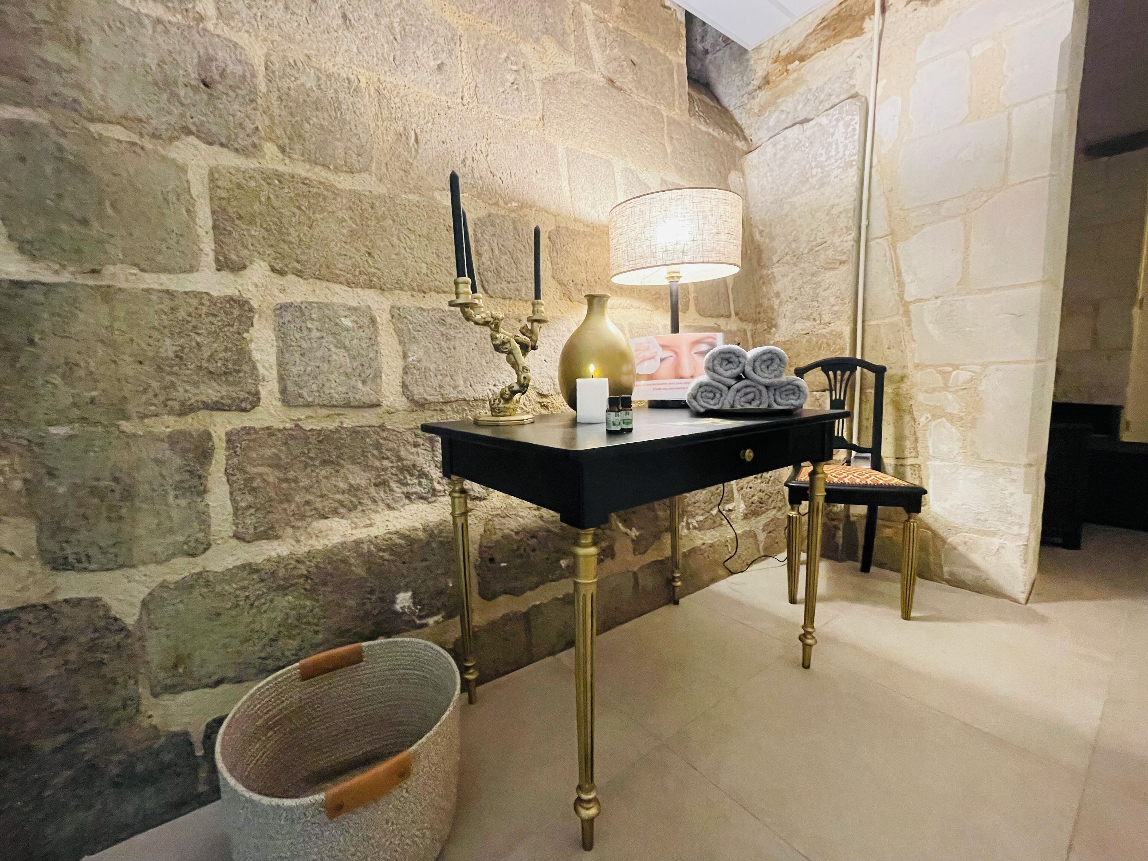 Un mur de pierre, une table noire avec une lampe, une bougie et une chaise.