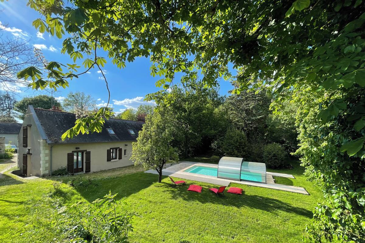 Uma casa com piscina, cercada por um gramado bem cuidado e árvores.