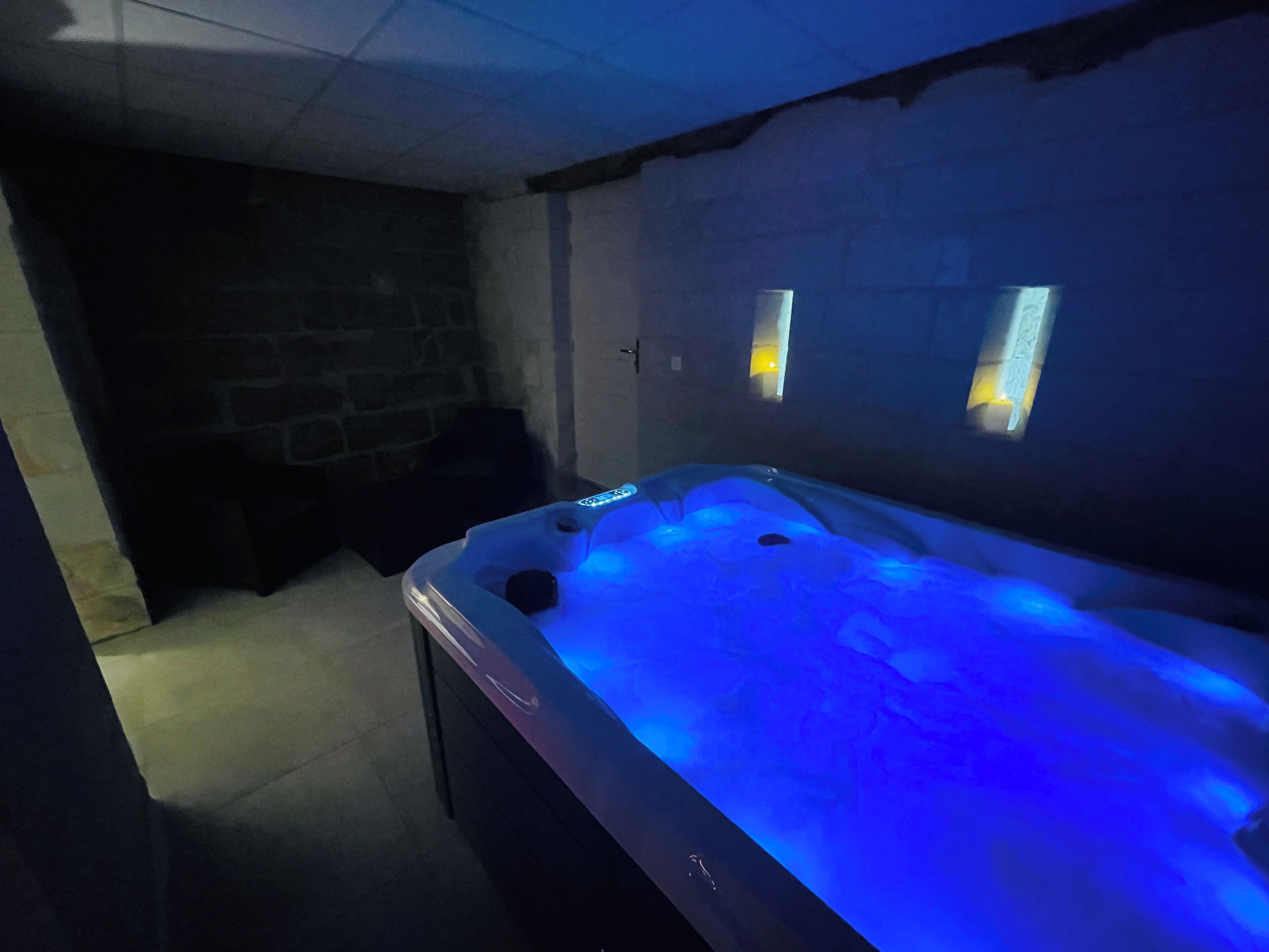 A spa room with a hot tub illuminated by blue lights, a stone wall, and a small window.