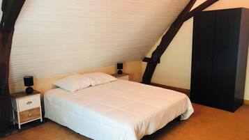 Una camera da letto con soffitto spiovente, un letto con biancheria bianca, due comodini con lampade e un armadio scuro.