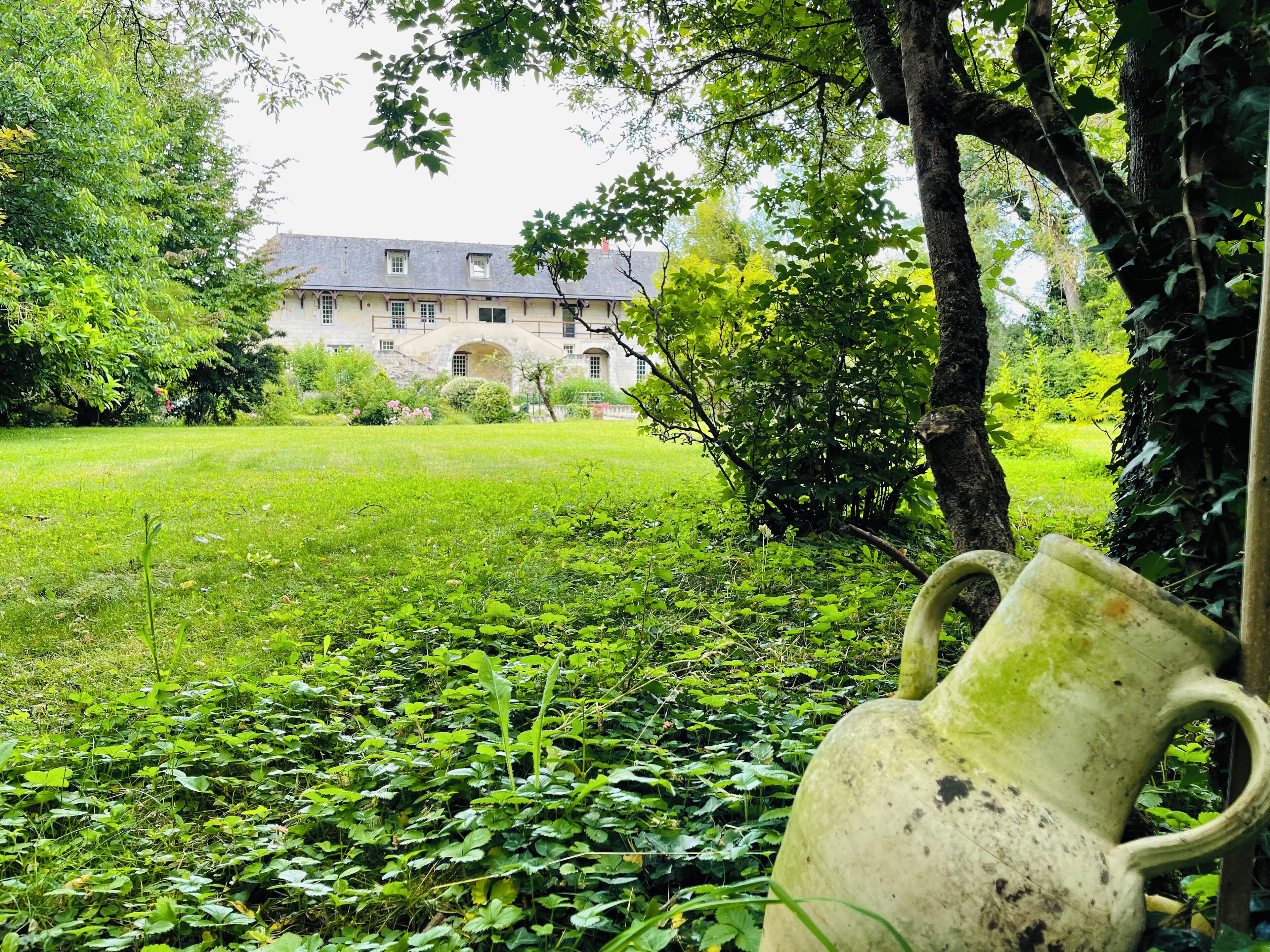A garden with a large building in the background, a tree, and a weathered vase in the foreground.