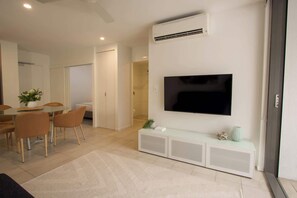 A modern living room with a flat-screen TV, a white console table, and a dining area with chairs and a table.