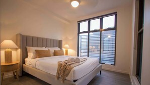 Ein ordentlich eingerichtetes Schlafzimmer mit einem großen Bett, zwei Nachttischen, einem Fenster mit Jalousien und einer Deckenleuchte.