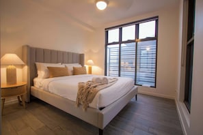 A neatly arranged bedroom with a large bed, two bedside tables, a window with blinds, and a ceiling light. - 2BR with Parking | Walk to QPAC & South Bank (South Brisbane)