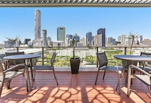 A balcony with a city skyline view, metal chairs, and a potted plant. - 2BR with Parking | Walk to QPAC & South Bank (South Brisbane)