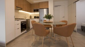A modern kitchen with a dining area, including a round table and four chairs, a built-in oven, microwave, and a refrigerator. - 2BR with Parking | Walk to QPAC & South Bank (South Brisbane)