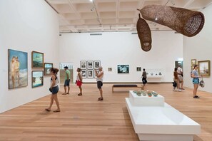 Eine Kunstgalerie mit Holzdielen, weißen Wänden und verschiedenen Kunstwerken.