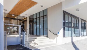 A modern building entrance with glass doors, a wooden ceiling, and a ramp leading to the entrance.