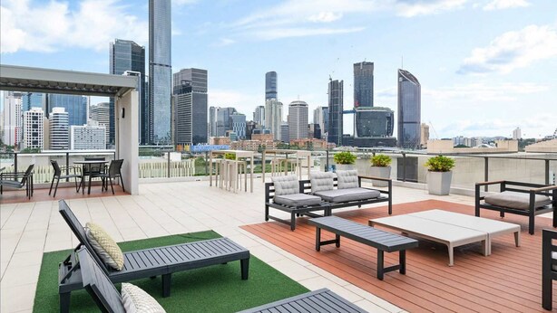 Eine Dachterrasse mit Sitzgelegenheiten im Freien, Blick auf eine Stadtlandschaft und ein modernes Gebäude im Hintergrund.