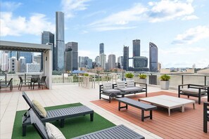 A rooftop terrace with outdoor seating, a view of a city skyline, and a modern building in the background.