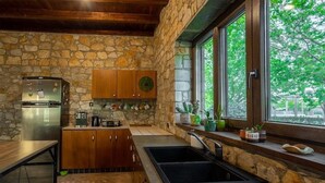 Una cucina con pareti in pietra, mobili in legno, frigorifero in acciaio inossidabile e una finestra vista su del verde.