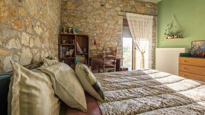 Una camera da letto con una parete in pietra, un letto con lenzuola a motivi, un comò in legno, una libreria e una finestra con tende.