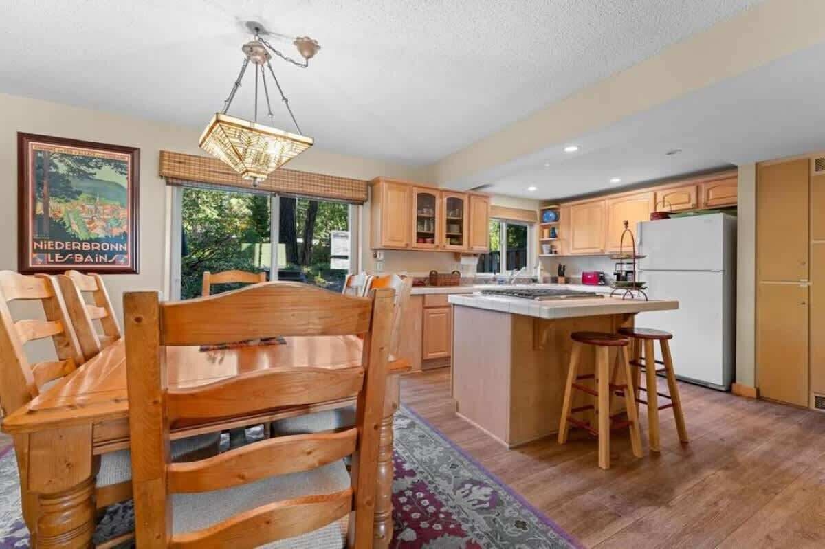 Una cocina con armarios de madera, un comedor con una mesa y sillas de madera, y una lámpara colgante.