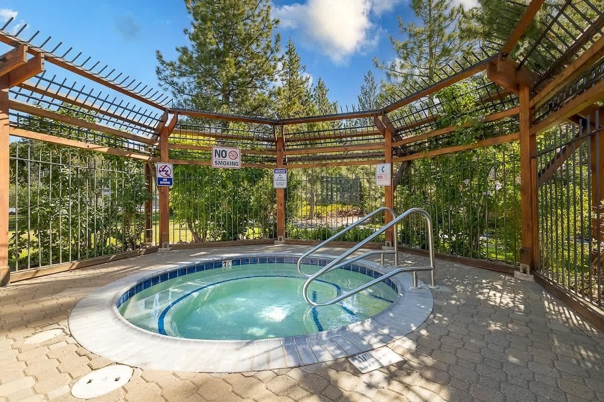 A hot tub area with a wooden pergola, a pool, and surrounding greenery.