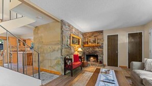 A living room with a fireplace, a sofa, a coffee table, and a staircase. - Two Story Townhome with Hot Tub, Walk to Lake (Tahoe City)