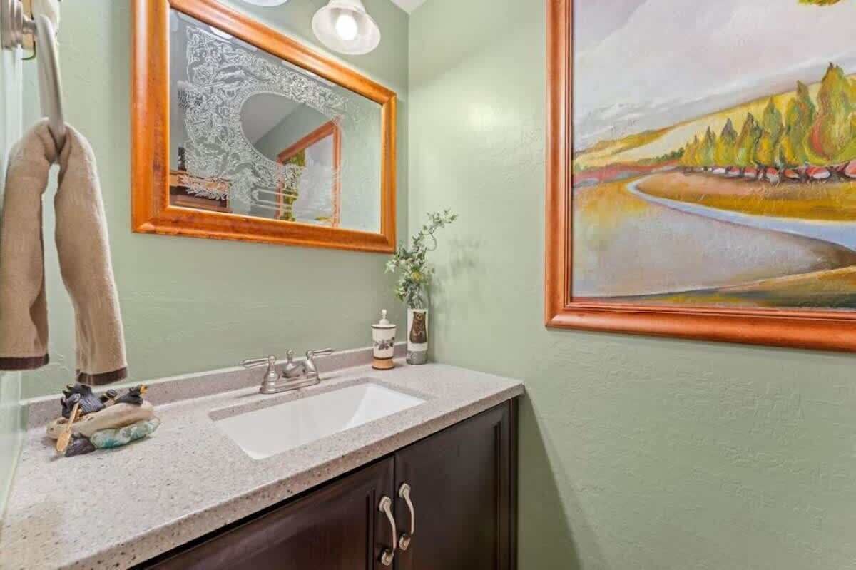 A bathroom with a sink, mirror, towel rack, and a painting on the wall.