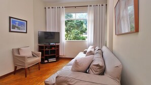 Ein Wohnzimmer mit einem beigefarbenen Sofa, einem Fernseher und einem Fenster mit Vorhängen.