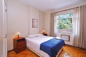 Una camera da letto con un letto, due comodini con lampade, una finestra con tende e un termosifone.
