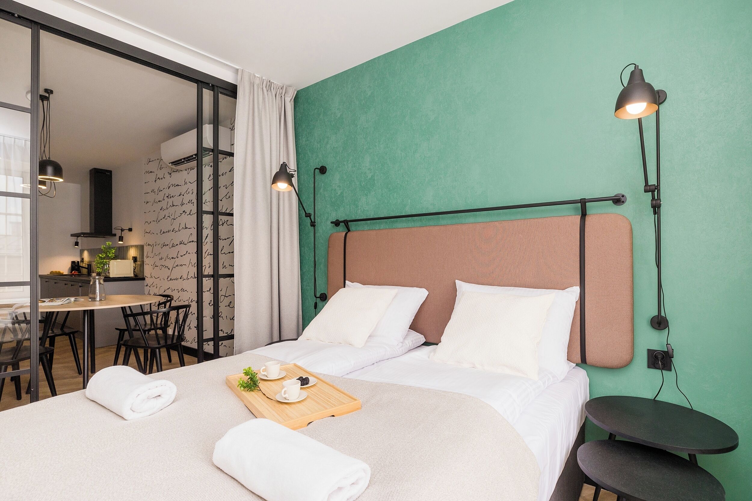 A hotel room with a bed, a small table with a tray of breakfast, a desk, and a chair.