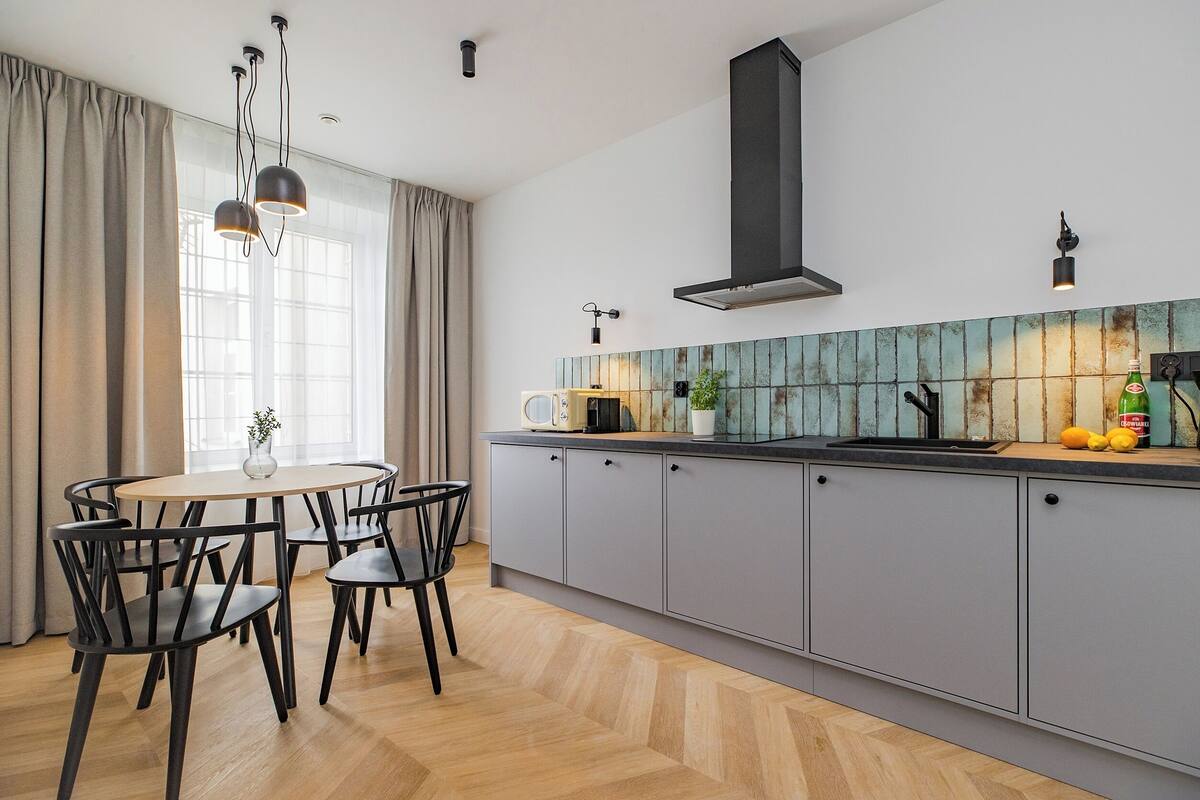 A modern kitchen with grey cabinets, a black range hood, and a window with sheer curtains.