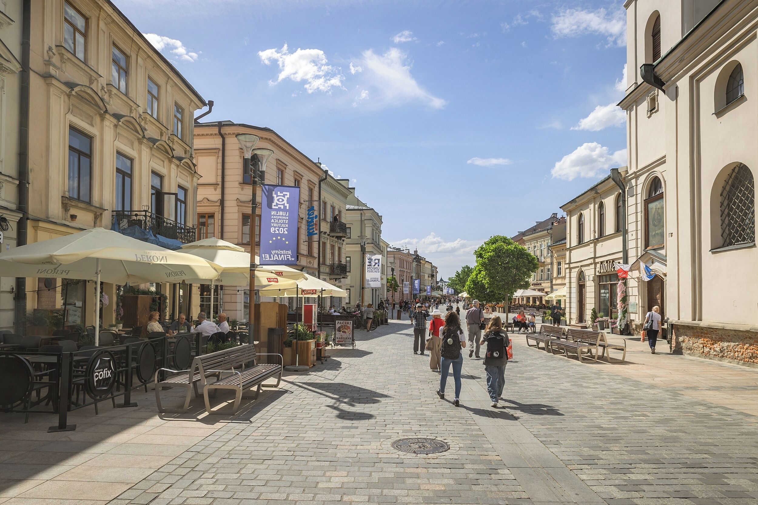 A pedestrian street lined with cafes and outdoor seating, with people walking and sitting.