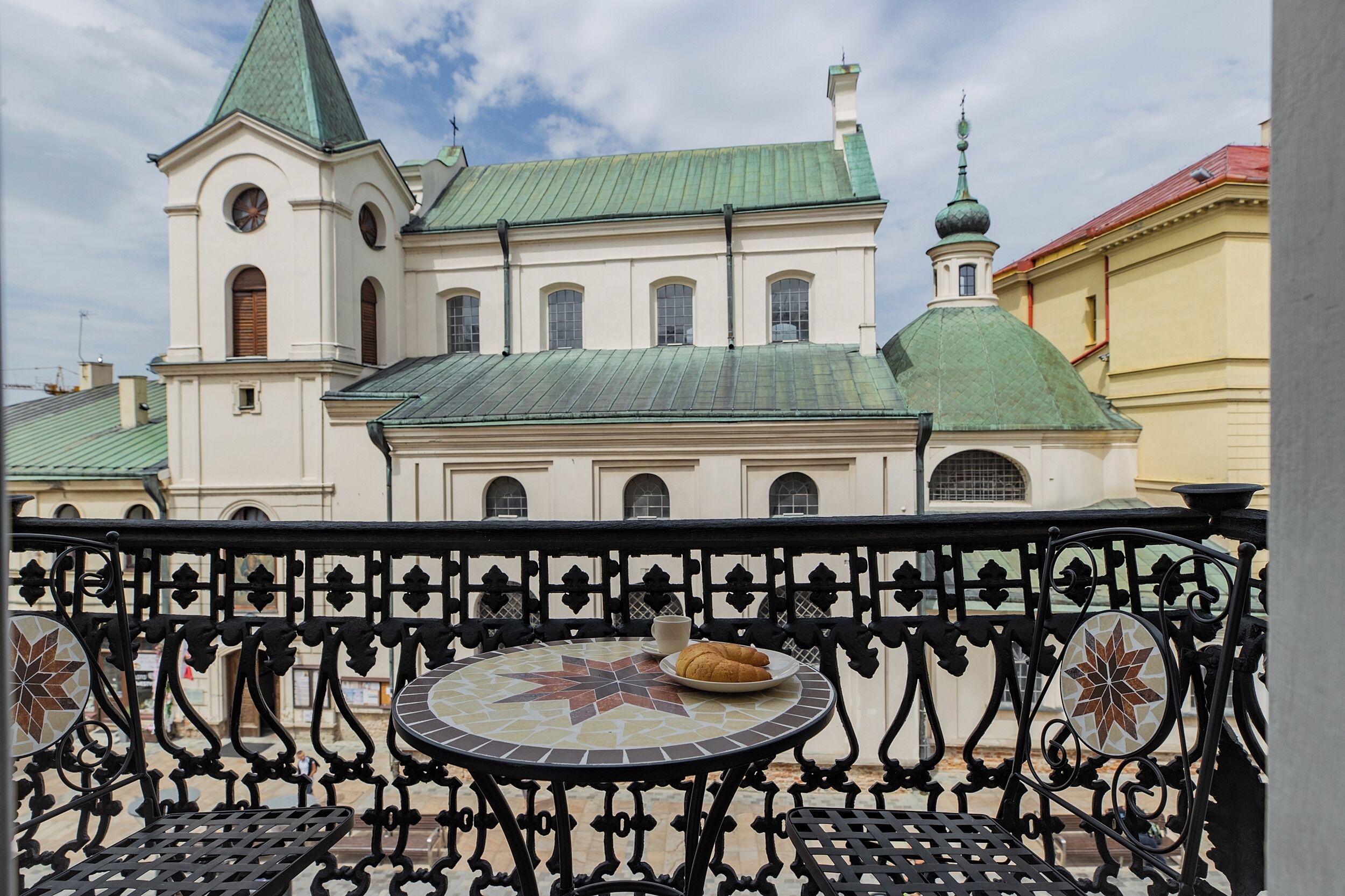 A balcony with a tiled table and chairs, overlooking a building with a green dome and a white facade.
