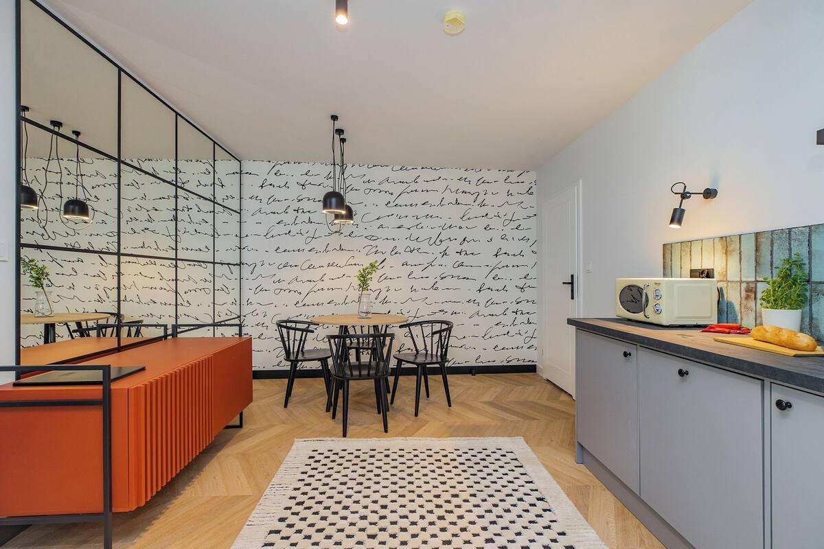 A modern kitchen with a dining area, featuring a patterned wallpaper, a built-in microwave, and a wooden herringbone floor.