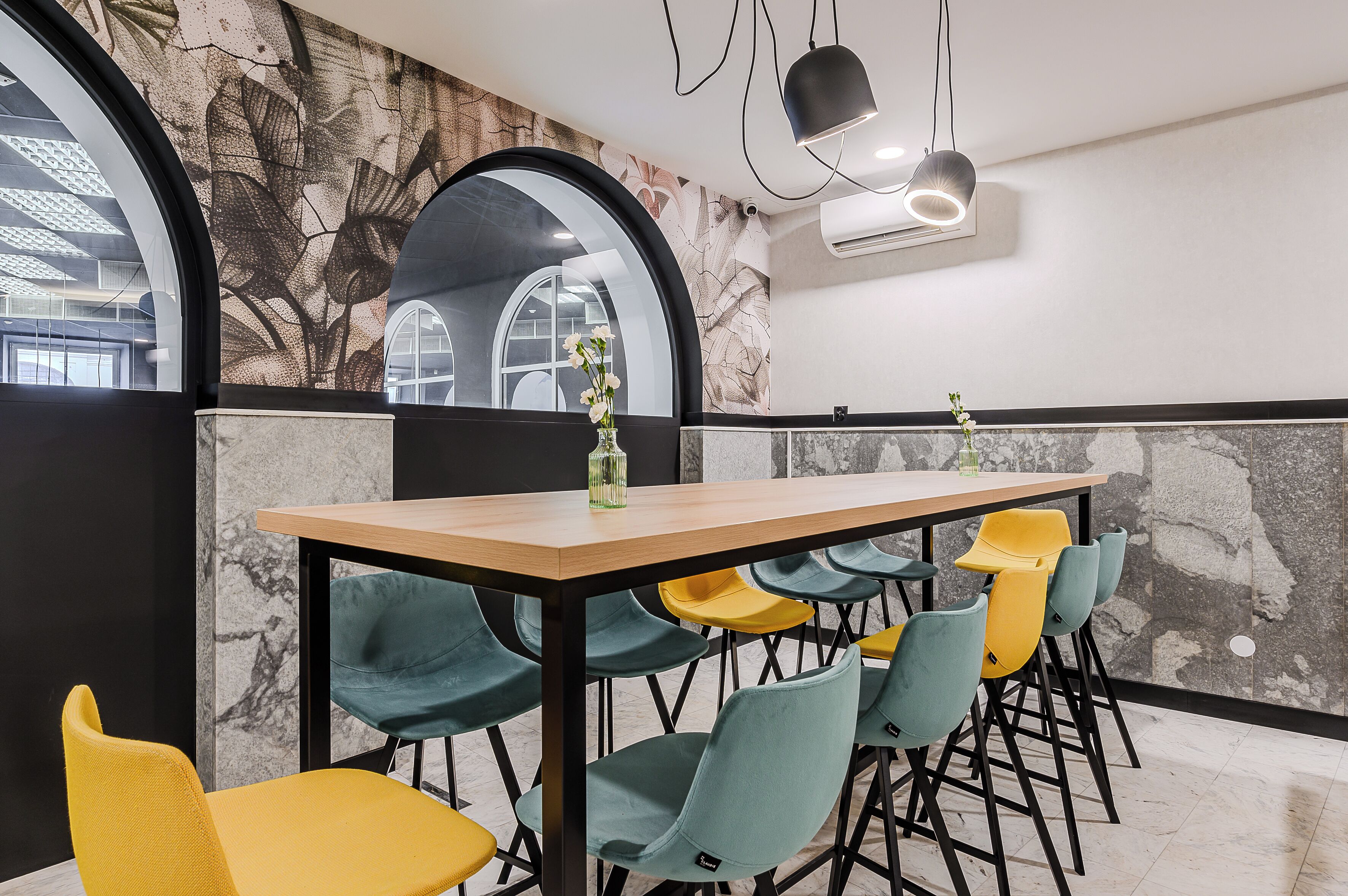 A modern meeting room with a marble wall, a wooden table, and colorful chairs.